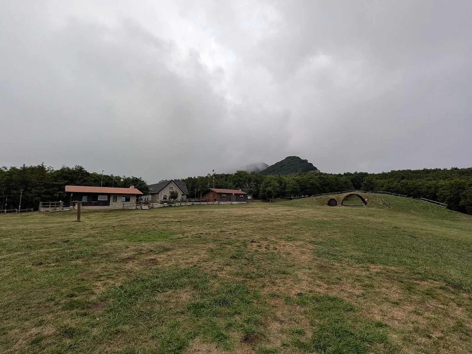 Il pianoro erboso di Prato Gentile a Capracotta con rifugi in pietra e legno, boschi e una cima montuosa fra le nuvole