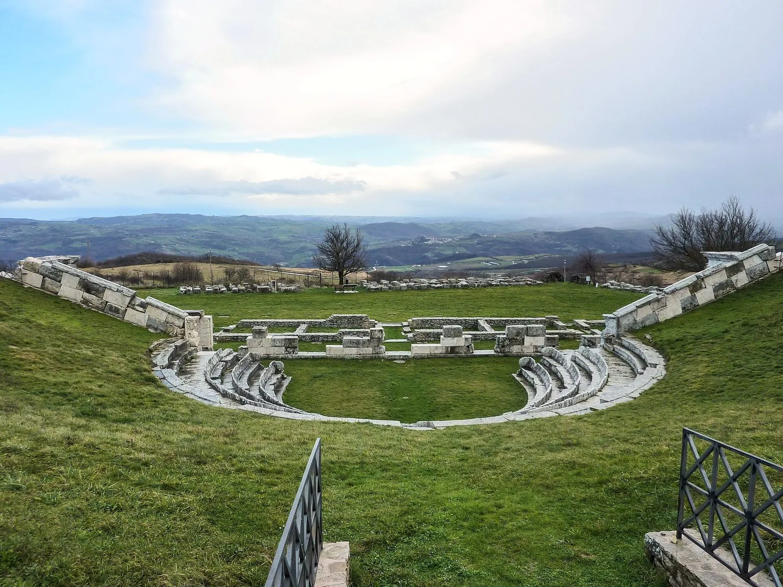 Il teatro sannitico di Pietrabbondante con le gradinate in pietra immerse nel prato e le colline dell'Alto Molise sullo sfondo